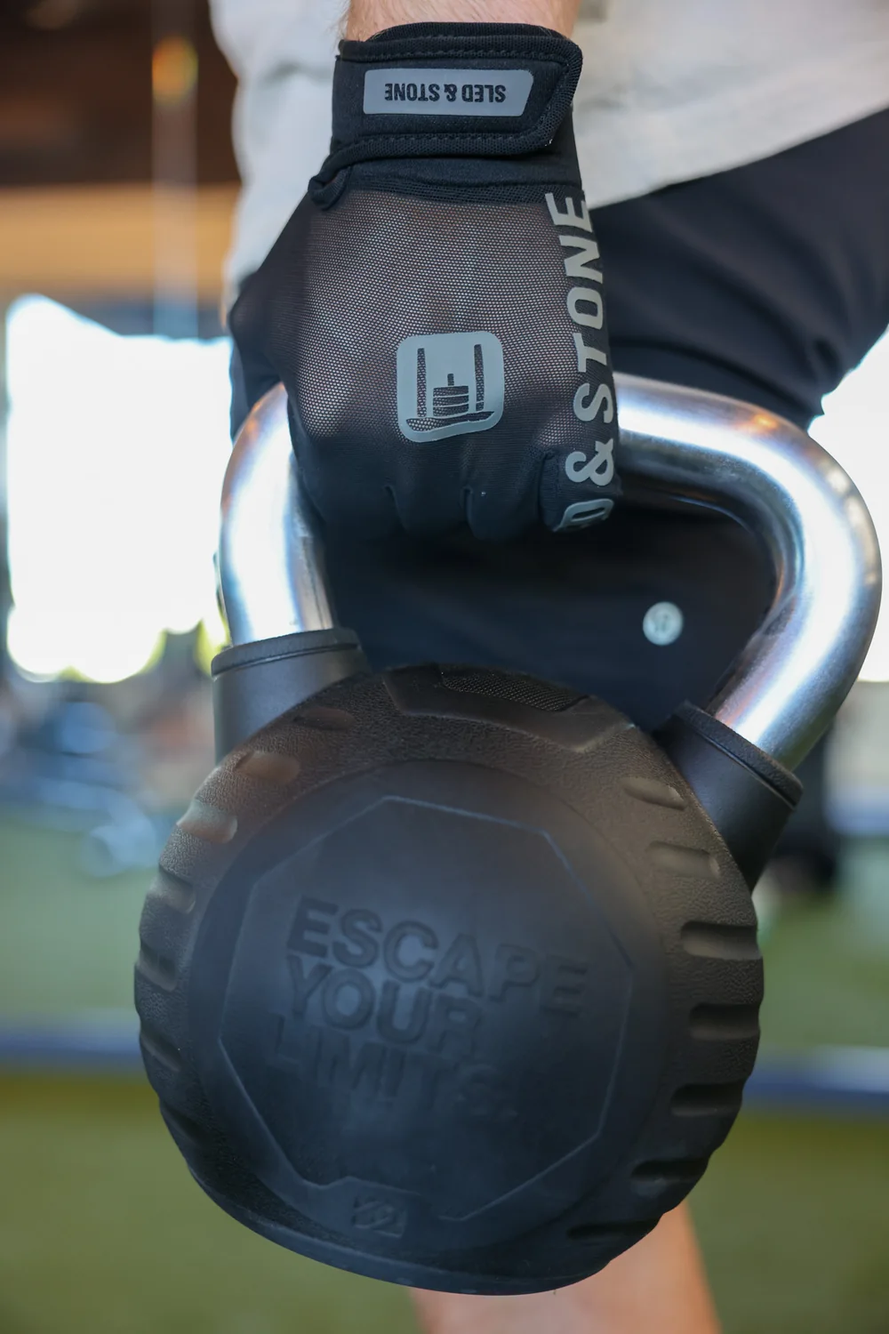 The Sled & Stone glove locked around a kettlebell handle, the sled mark and wordmark across the back of the hand