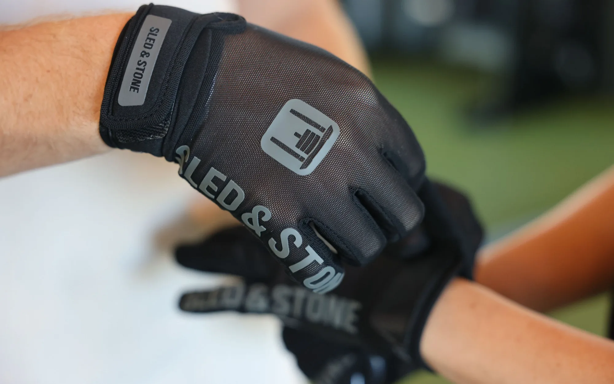 Fastening the wrist strap of the Sled & Stone glove, the sled mark and wordmark across the back of the hand
