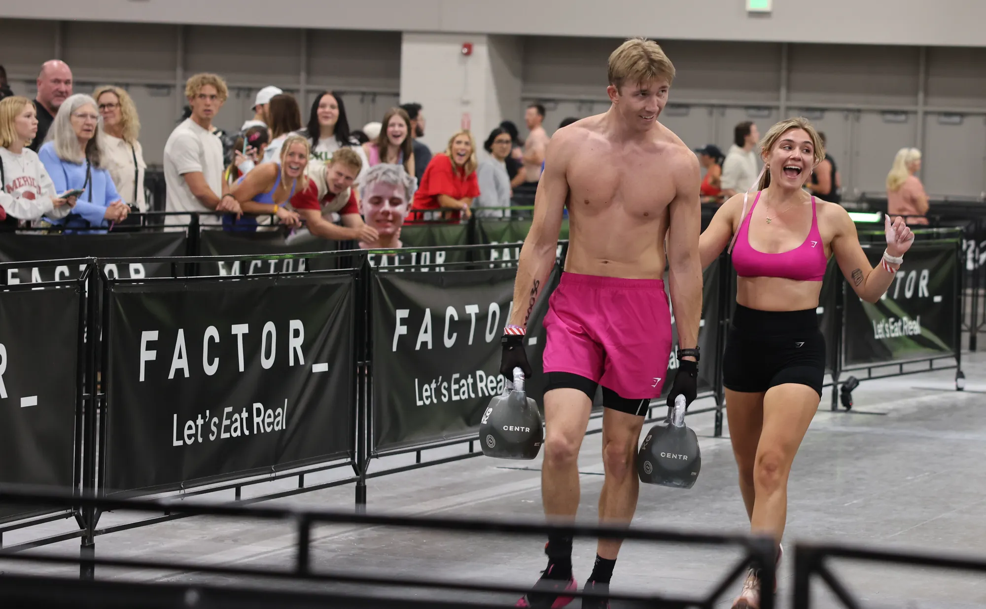 Zach Taylor on the farmer's carry at HYROX Salt Lake City, a kettlebell in each gloved hand, the crowd cheering behind him