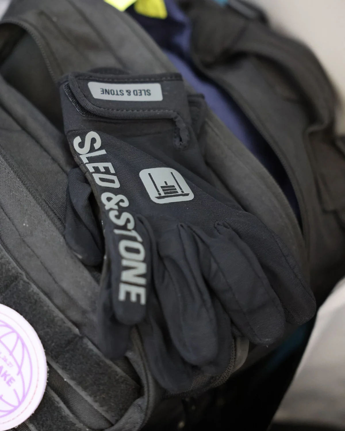The Stonegrip Glove on a hand gripping a kettlebell handle: wrist tag, sled mark and wordmark down the finger — view 6