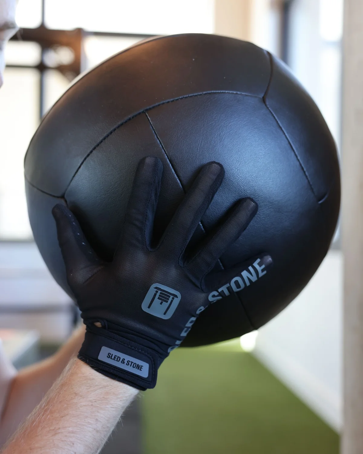 The Stonegrip Glove on a hand gripping a kettlebell handle: wrist tag, sled mark and wordmark down the finger — view 3