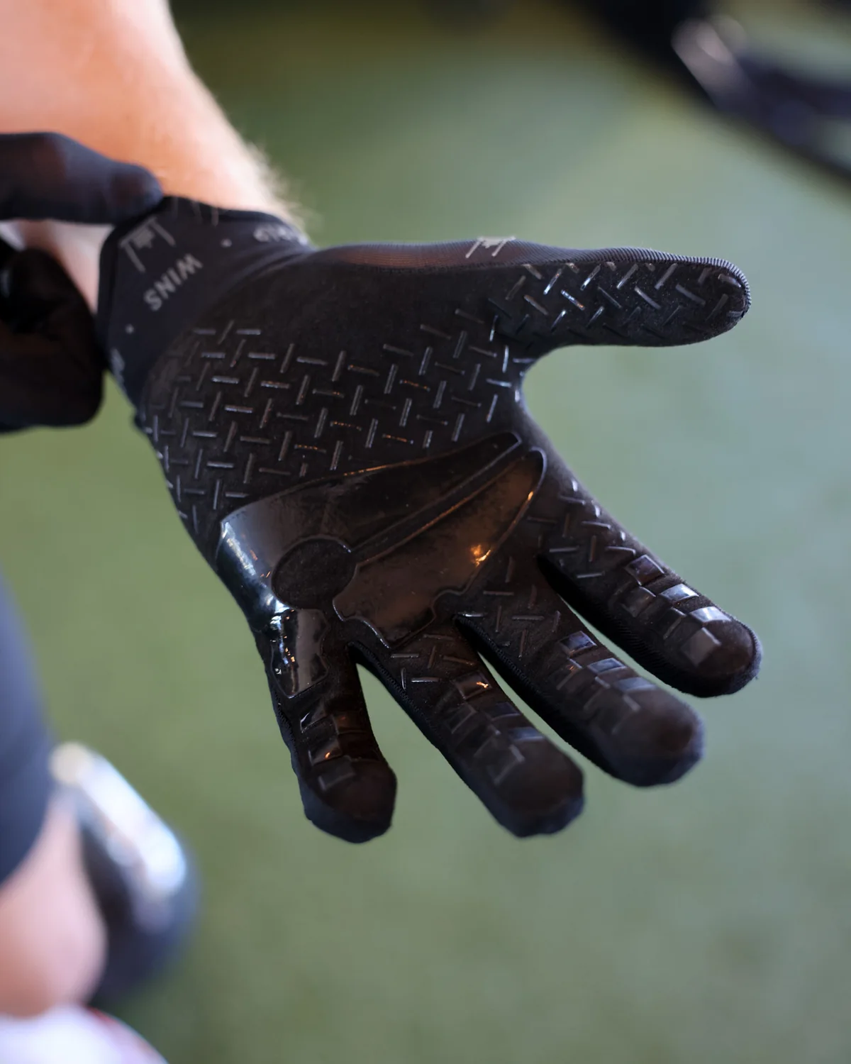 The Stonegrip Glove on a hand gripping a kettlebell handle: wrist tag, sled mark and wordmark down the finger — view 2