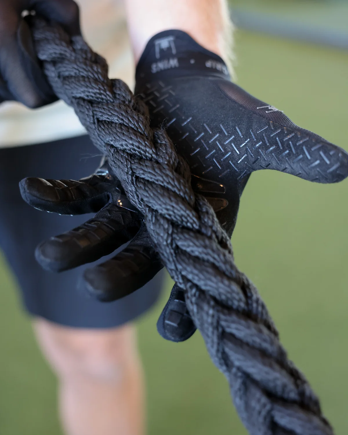 The Stonegrip Glove on a hand gripping a kettlebell handle: wrist tag, sled mark and wordmark down the finger — view 5