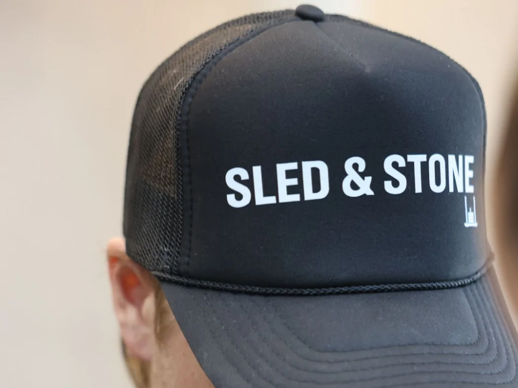 The black Sled & Stone trucker, laid on turf, Sled & Stone printed across the front — view 4