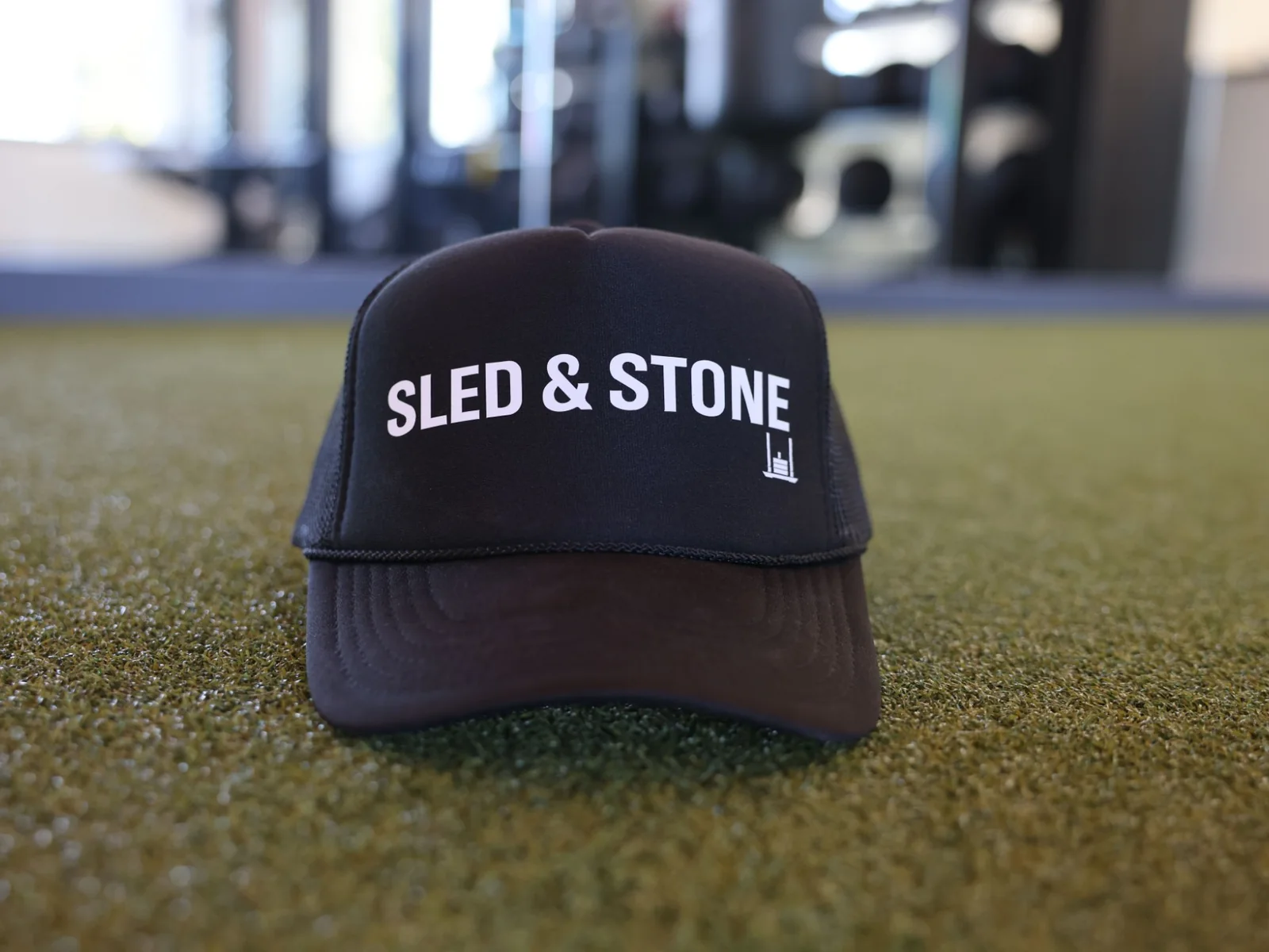 The black Sled & Stone trucker, laid on turf, Sled & Stone printed across the front — view 3