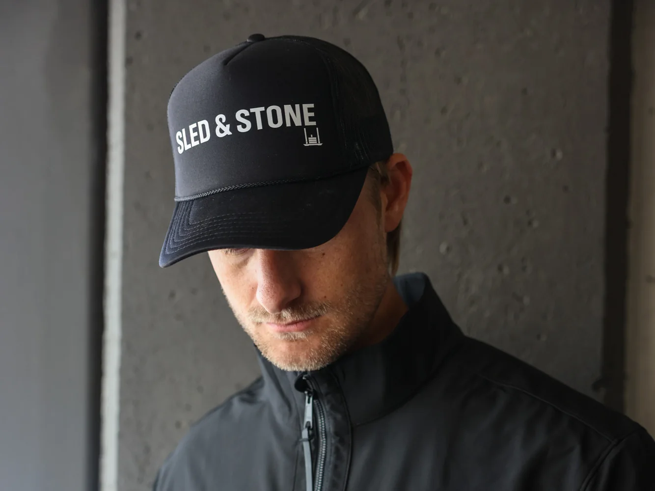 The black Sled & Stone trucker, laid on turf, Sled & Stone printed across the front — view 2