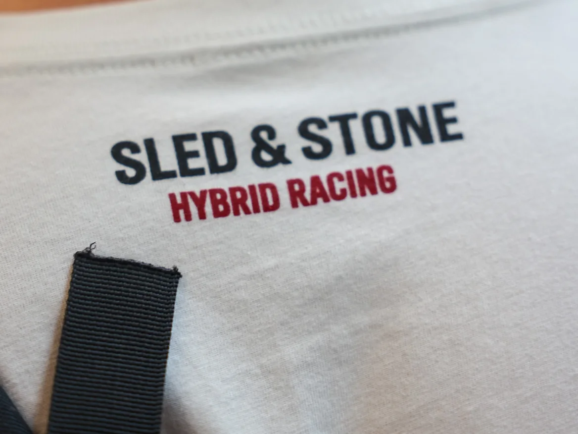 The Grip Wins Races tee in black and sand, worn side by side: Sled & Stone across the chest over Grip Wins Races — view 5